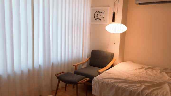 暖かいベージュとナチュラルな色調の寝室、アームチェアとオットマン、バブルランプが配置された雰囲気のあるインテリア