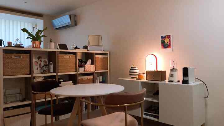 A living room with white and wood tones featuring a bookshelf with rattan baskets and a round dining table in a natural and simple style