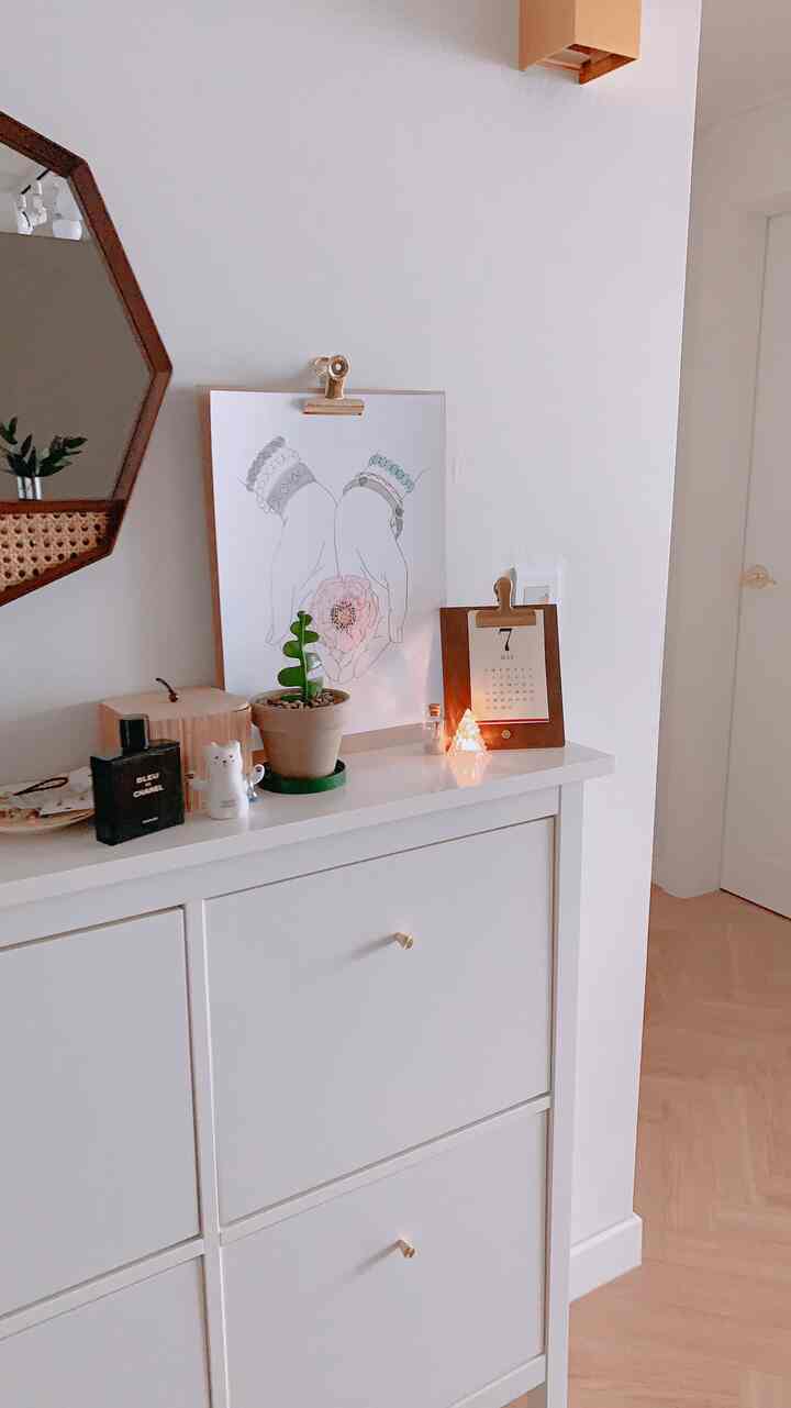 明るいホワイトトーンのシューズラックの上に額縁、カレンダー、植物とミニチュアが配置された落ち着いたインテリアスペース