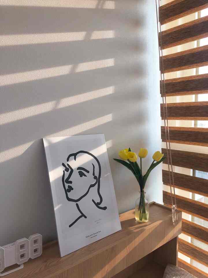 ナチュラルカラーの小さなデスクスペース、黄色い造花のチューリップとモダンな黒白スケッチが配置された落ち着いた雰囲気のインテリア