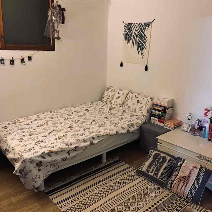 Cozy bedroom with natural tones featuring floral bedding, hanging fabric poster, books, and a patterned rug