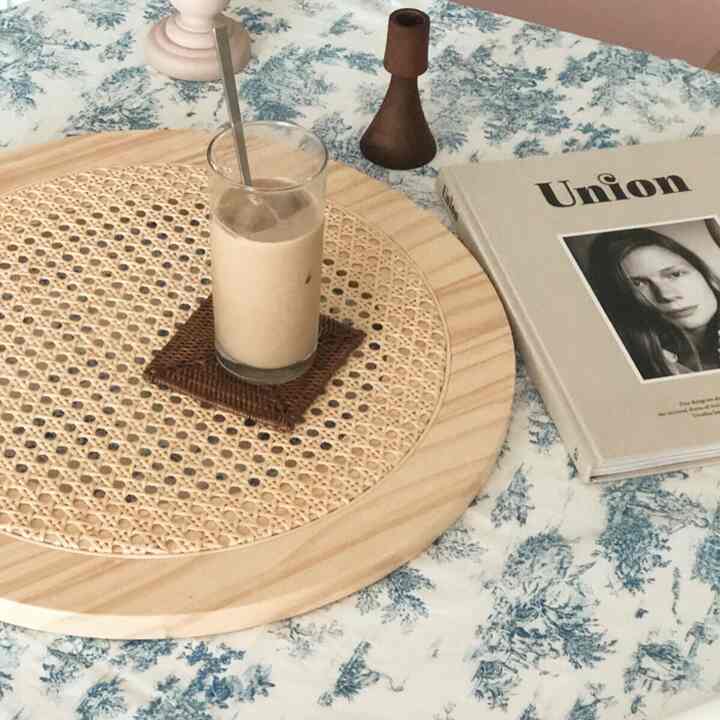 パステルトーンのフレンチカントリー風キッチンテーブル、ラタンのトレイとガラス、花柄のテーブルクロスが配置された雰囲気のあるインテリア