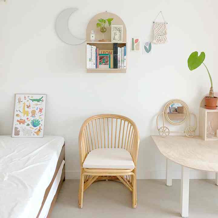 A kids' room with white walls and wood tone furniture, featuring a rattan chair and mirror with charming decorative elements in a natural style