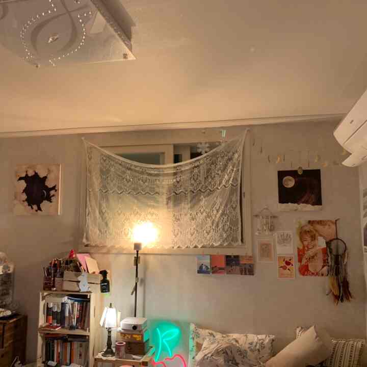 White and beige toned bedroom featuring sofa, lace curtains, and vintage posters, creating a cozy atmosphere