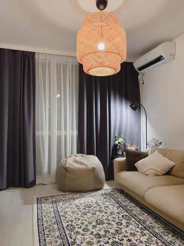 A warm beige-toned living room featuring a beige sofa, bean bag, and blackout curtains creating a cozy ambiance