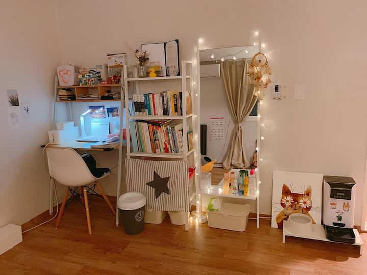 Natural wood tone floor studio apartment with white furniture, mirror, and string lights in a cozy home office setup