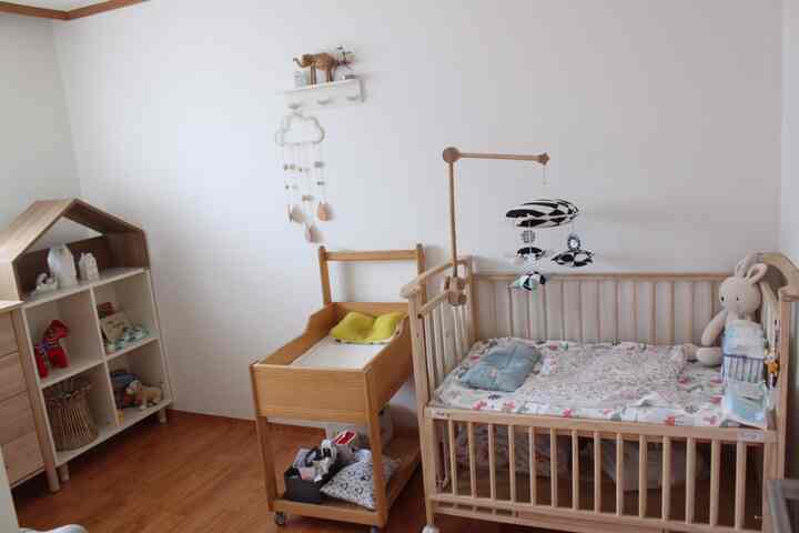 White walls and wood-toned furniture in a kids' room featuring a baby crib and changing table with a warm atmosphere