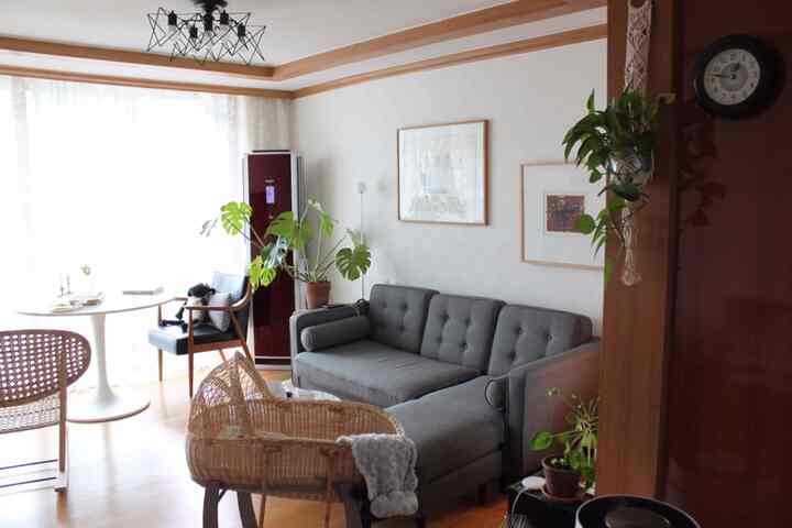 Bright natural living room with gray sectional sofa, wood tone flooring, round dining table, and rattan rocking chair