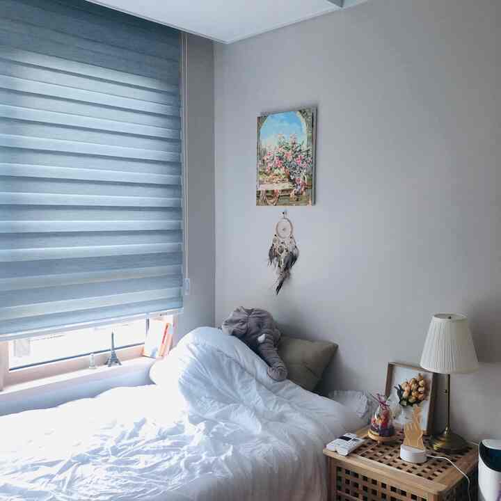 白とベージュの色調のワンルーム寝室、ナチュラルな木製収納テーブルと清潔な寝具が配された雰囲気のある空間