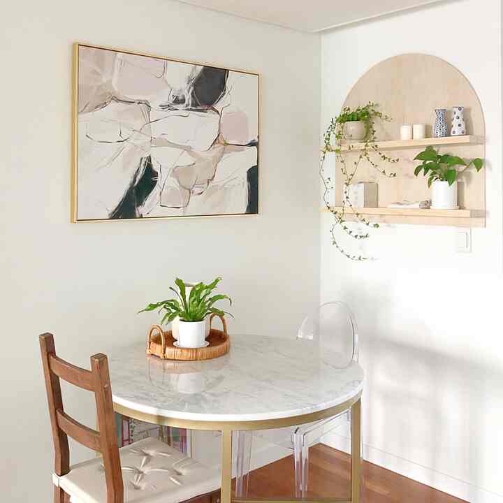 Natural wood tones and white background kitchen featuring a round marble dining table with mixed chairs and a large framed art piece creating a cozy atmosphere