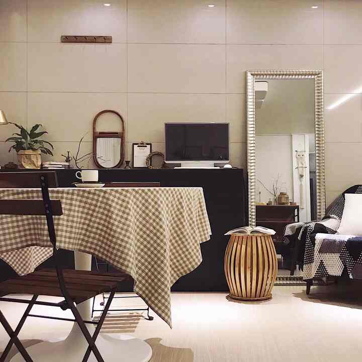 Natural wood tone living room featuring a checkered tablecloth, rattan mirror, and bamboo stool with cozy atmosphere