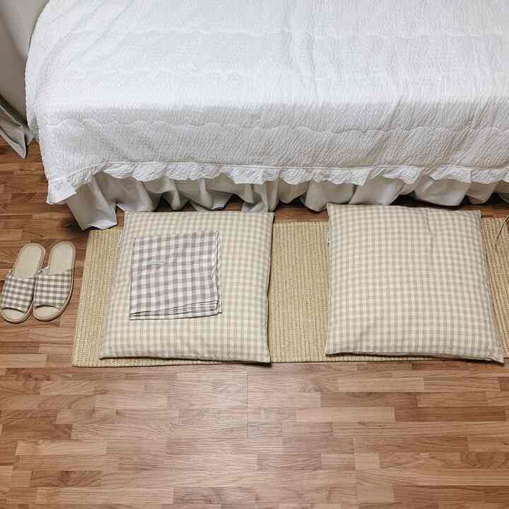 Beige and white toned studio apartment bedroom featuring checkered cushions, a rug, and plain slippers in a cozy natural setting