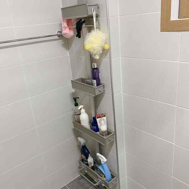A light gray-toned bathroom corner featuring a functional metal shelf neatly organizing various toiletries in a clean space.