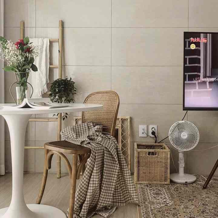 A living room with white and wood tones, featuring a rattan chair, round white table, and checkered cloth in a natural interior style
