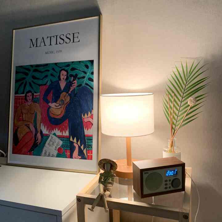 A cozy bedroom featuring natural color walls, wood tone nightstand with a table lamp, Britz speaker, wooden figurine, and plant for warm ambiance