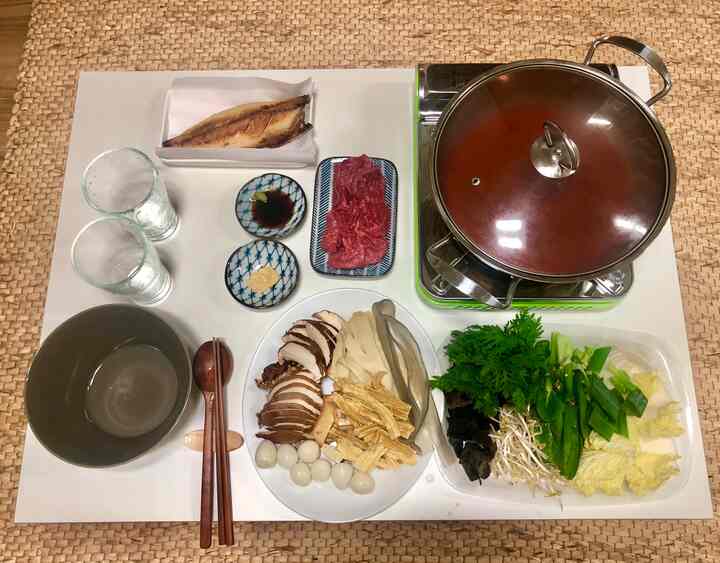 Natural beige and brown toned studio apartment dining table featuring rattan mat base, bowl set, and hot pot meal arrangement