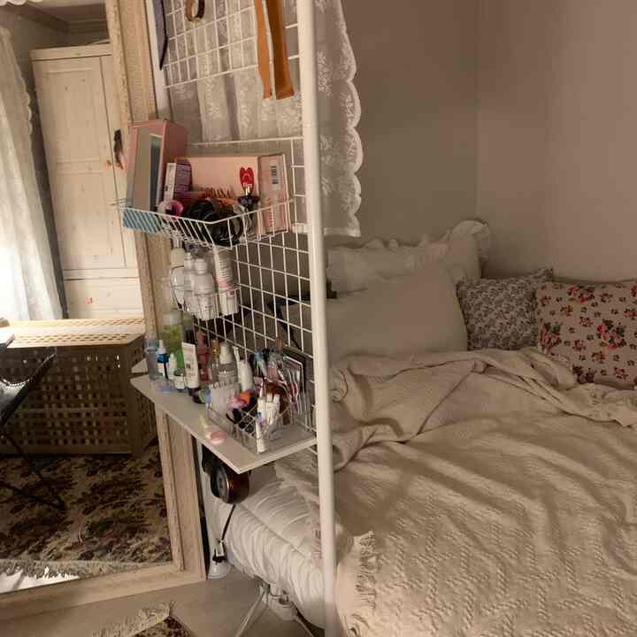 Cozy studio apartment small room in warm beige and white tones, featuring a bed with cushions and a vanity integrated into a room divider