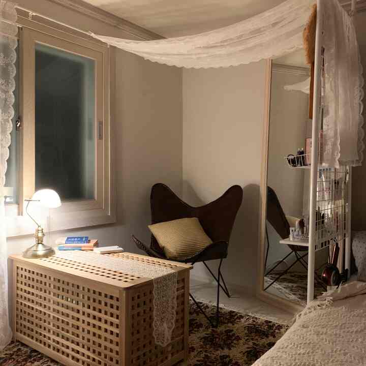Natural-toned studio bedroom featuring a large standing mirror, wooden storage box, and brown butterfly chair arranged cozy