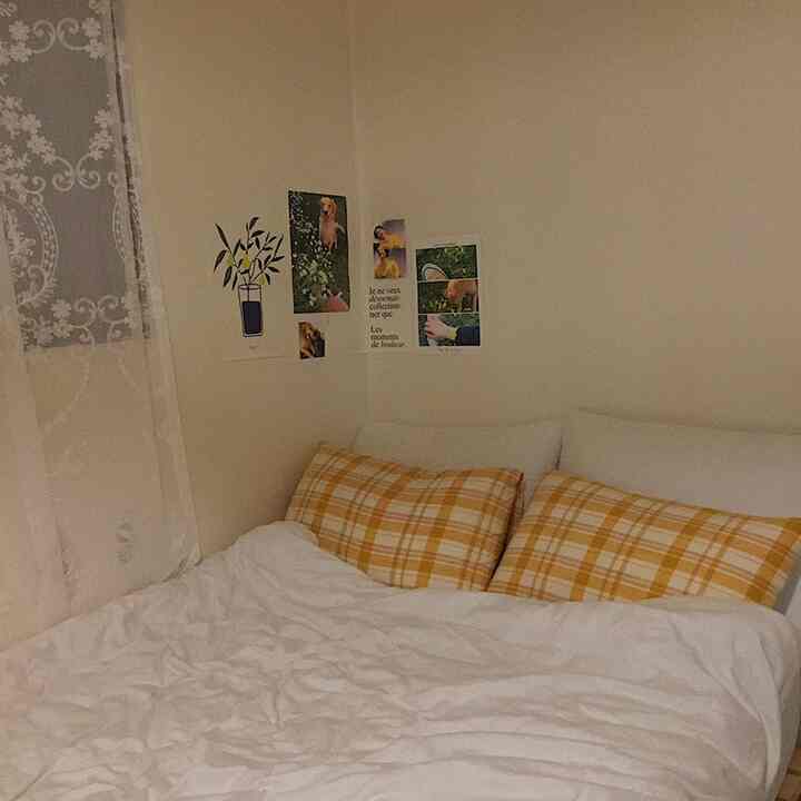 白と黄色のトーンのワンルーム寝室、レースカーテンとヴィンテージチェックの枕が配置された雰囲気のあるインテリア