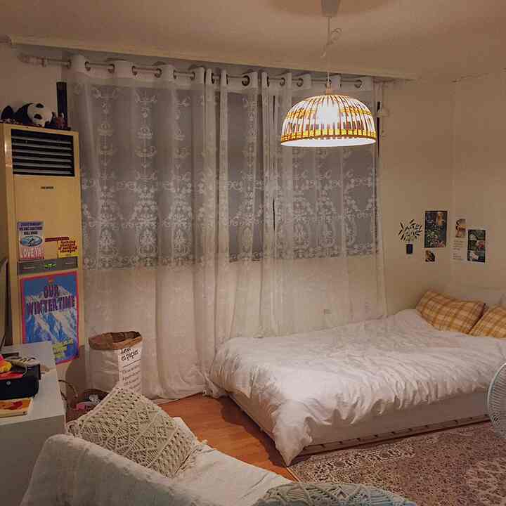 白と茶色を基調としたワンルーム寝室、ボヘミアンスタイルのラグとマクラメソファが配置された雰囲気のある空間