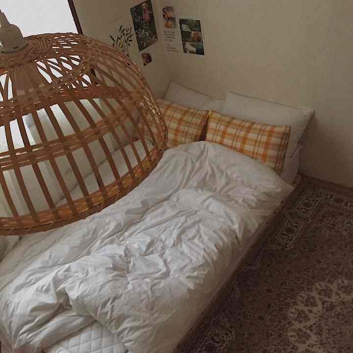 暖かいナチュラルトーンのワンルーム寝室、ラタン照明とオレンジのチェック柄枕が配置された居心地の良い空間