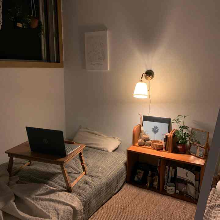 Natural wood tone single bedroom featuring a folding desk with laptop and a wall sconce lamp, creating a cozy compact room