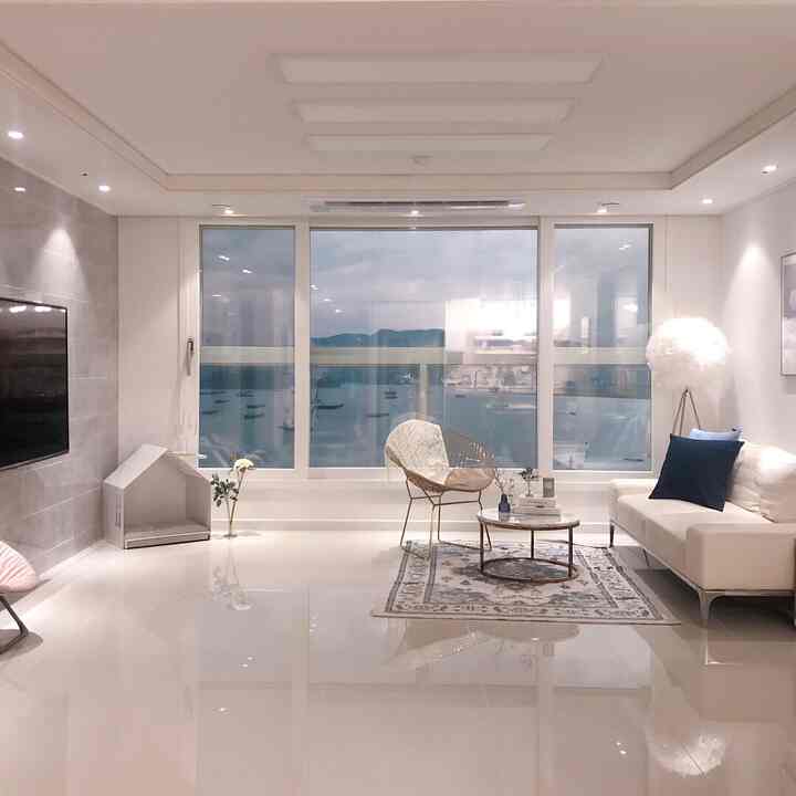 White-toned living room featuring large windows, modern sofa, armchair, and rug with a clean and simple atmosphere