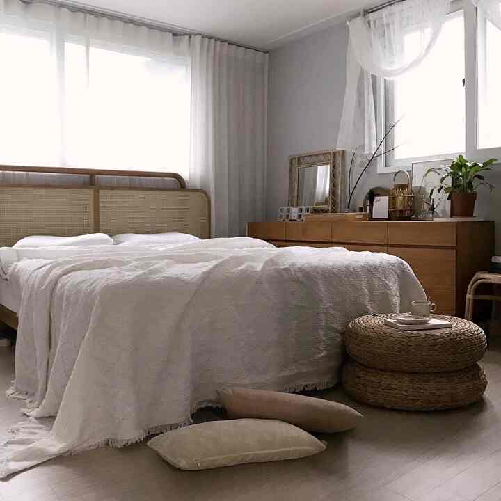 Natural toned bedroom featuring a cane bed, teak sideboard, and white linen curtains with a cozy atmosphere