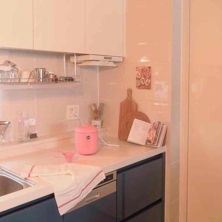 ピンクとホワイトの色調のコンパクトなキッチン。マカロン型炊飯器と木製まな板が配置された、清潔感のあるキッチンインテリア