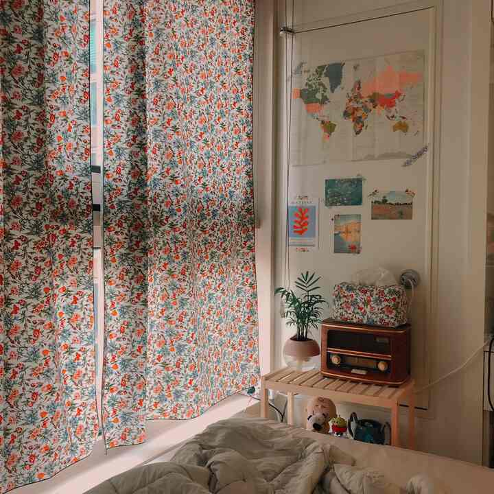赤い花柄のカーテンとナチュラルな木製棚が配置された雰囲気のある寝室