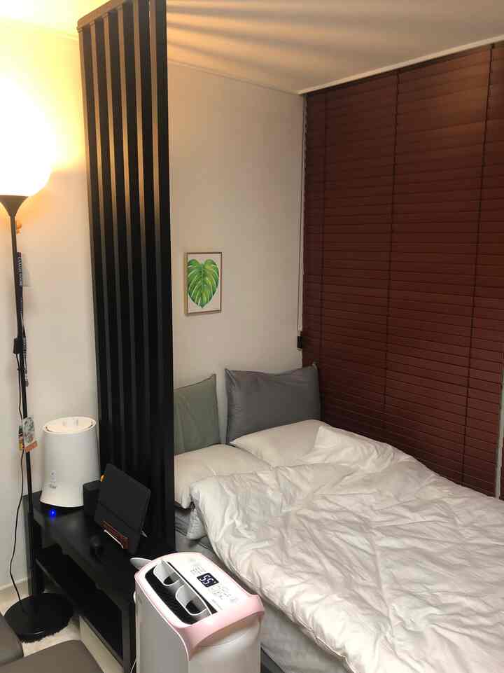 White-toned studio bedroom with brown blinds, bed, and partition wall creating a cozy and calm atmosphere