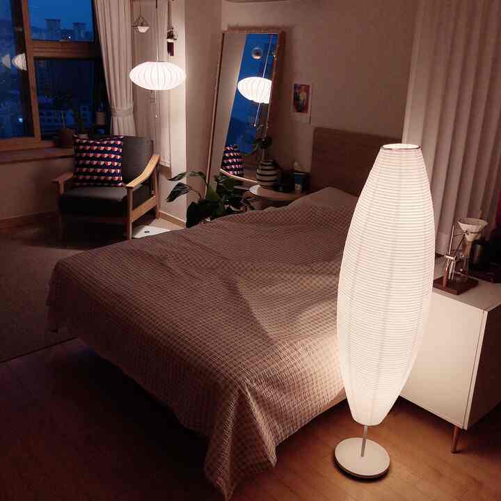 温かみのあるホワイトとナチュラルウッドのワンルーム寝室、柔らかな照明と居心地の良いアームチェアが配置された印象的な空間