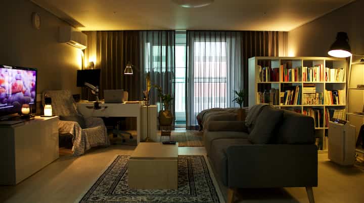 Modern living room in gray and white tones with light brown accents, featuring a sofa, bookshelf, and a remote work desk, creating a cozy atmosphere