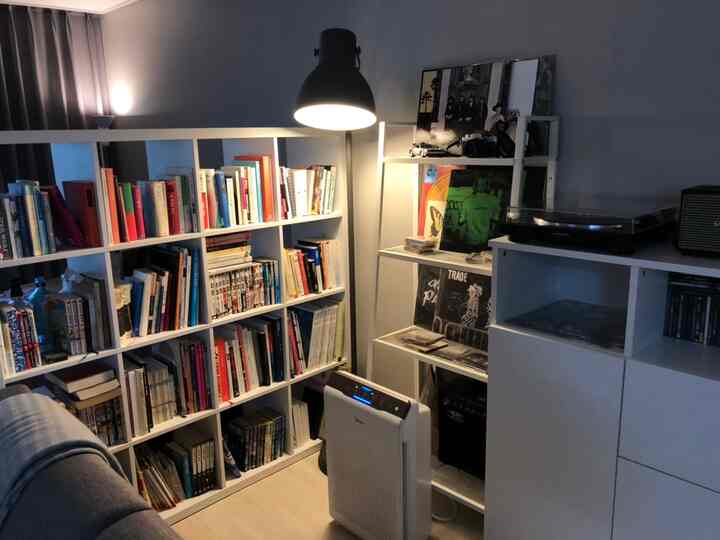 Modern living room in white with dark-toned lighting, featuring a bookshelf and floor lamp creating a cozy reading space