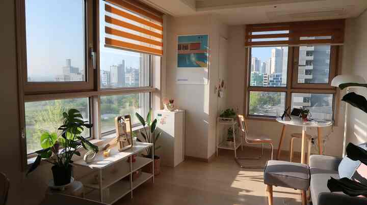 Natural modern studio apartment with warm wood tones, white walls, multifunctional table, and plants in a bright living space