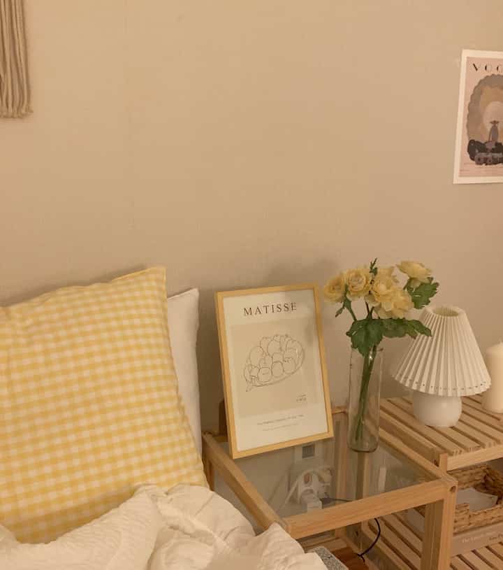 ベージュの壁とナチュラルな木製ナイトテーブル、花瓶と暖かい照明が配置された寝室のインテリア