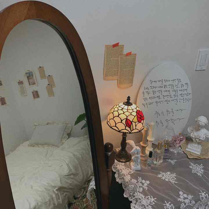 White and natural toned bedroom featuring a wooden full-length mirror and vintage lace-covered table with candles and vanity items, creating a cozy atmosphere