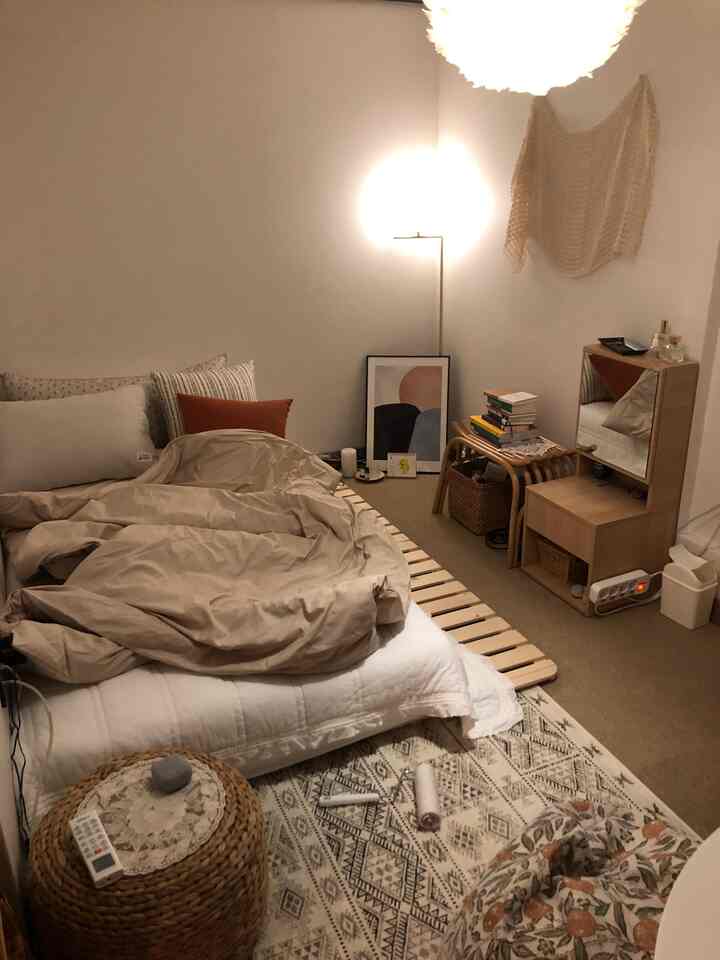 ベージュとウッドトーンが調和するコンパクトな寝室、木製ドレッサーとフロアランプが配置されたナチュラルな雰囲気のインテリア