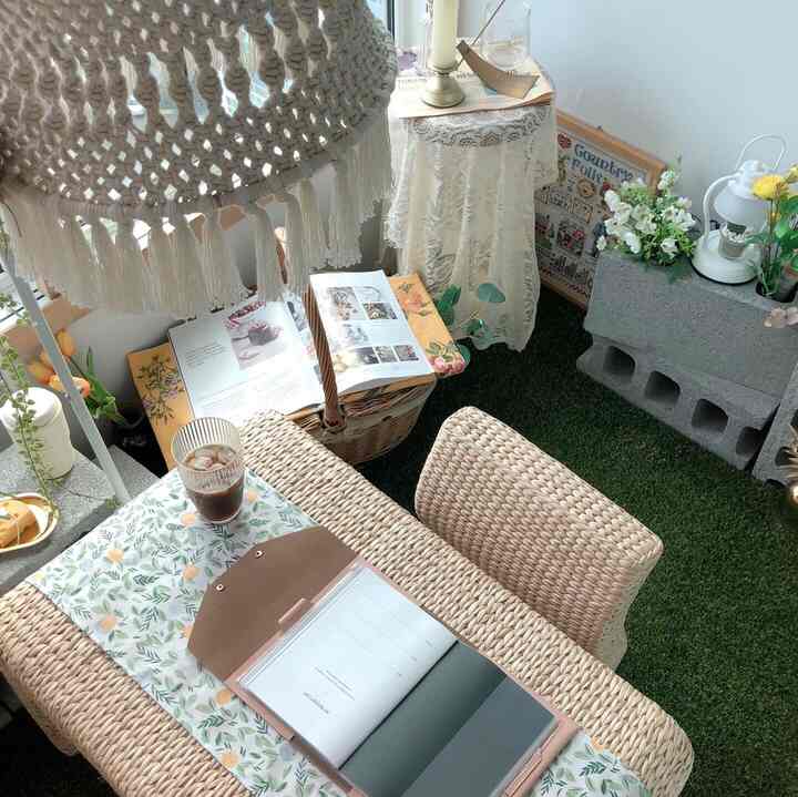 Natural tone veranda featuring rattan table and chairs, artificial grass floor, and various plants creating a cozy atmosphere