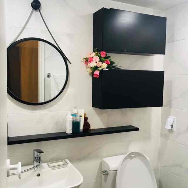 White-tiled bathroom featuring black cabinets and floating shelf, round mirror creates a clean and modern space
