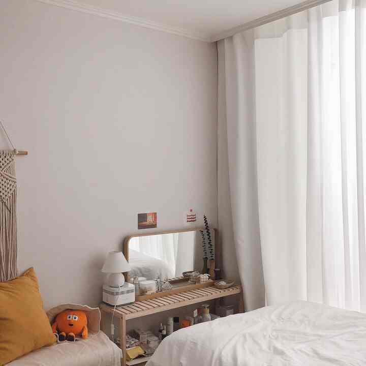 White and natural toned studio bedroom featuring a wooden vanity and white curtains, creating a cozy atmosphere