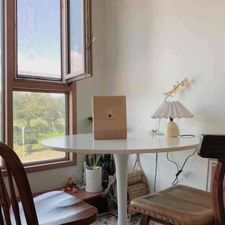 白とウッドトーンのワンルームダイニング、丸テーブルと木製チェア、植物とテーブルランプが配置された雰囲気のある空間