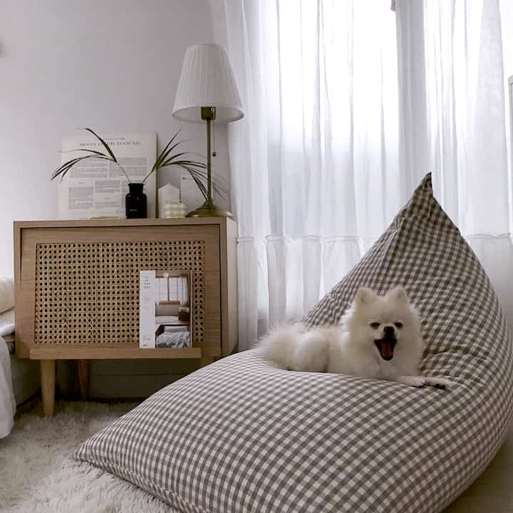 ナチュラルな色調のリビング、グレーのチェック柄ビーズクッションと白い犬がくつろぐ雰囲気のあるインテリア