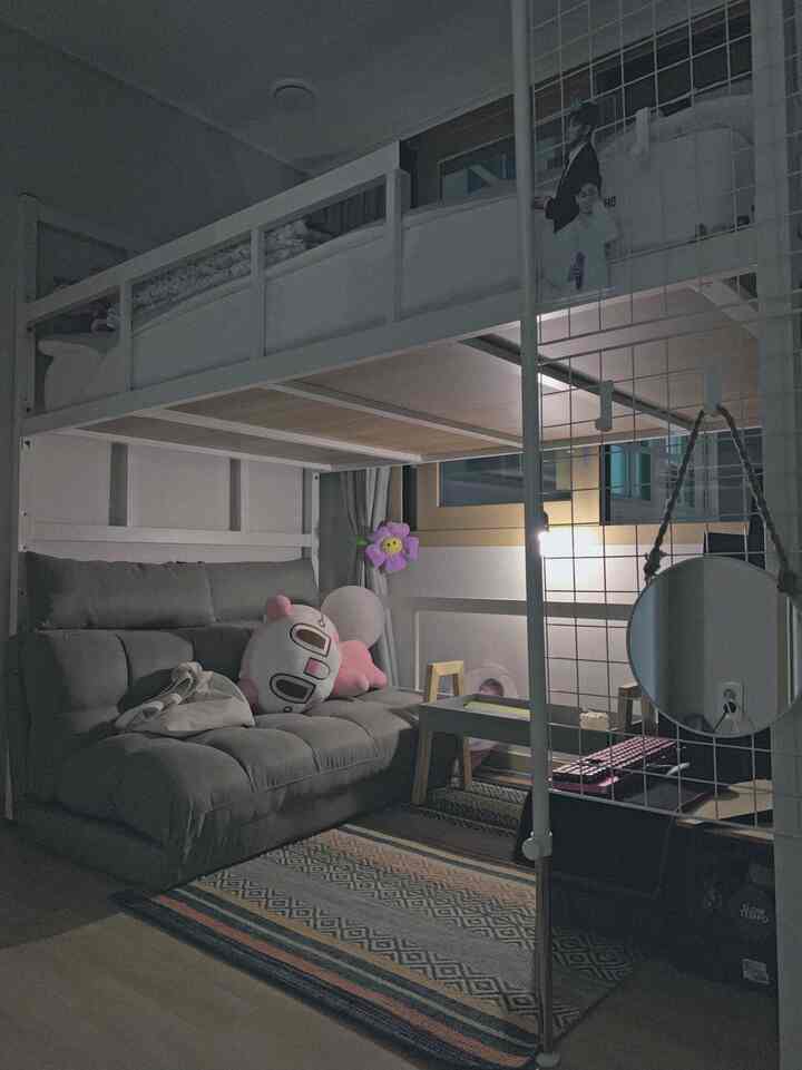 Calm gray and white toned small bunk bed room featuring sofa bed, rug, wall lamp, and desk in natural modern style