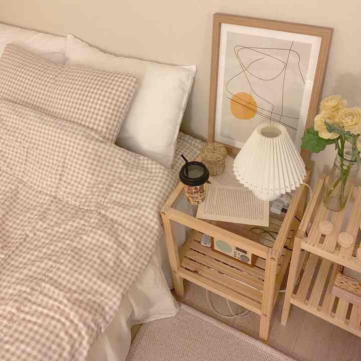 ベージュと木目調の寝室、チェック柄の掛け布団と枕、木製サイドテーブルと額縁が配置された温かみのあるインテリア