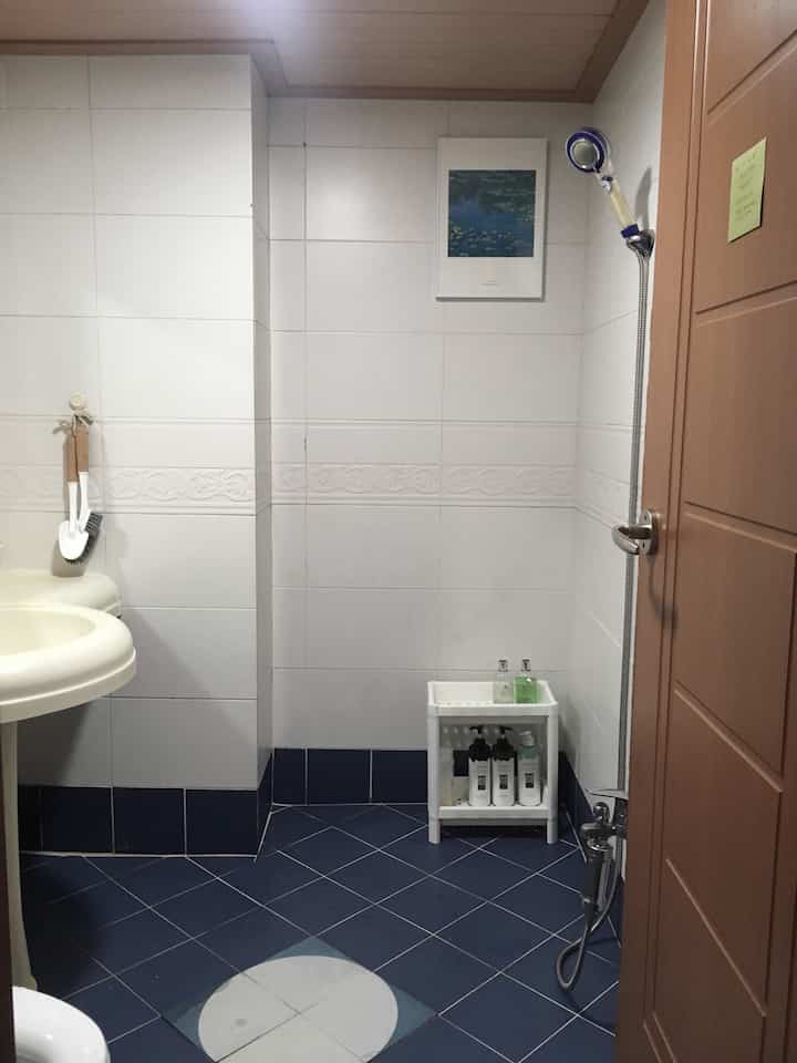 A clean bathroom in white and blue tones featuring a Monet artwork and bathroom shelf with toiletries
