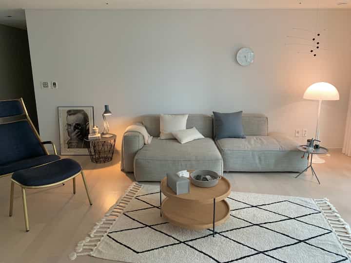 Natural beige-toned living room featuring a central sofa and round coffee table, with a blue armchair and lamps on left and right sides