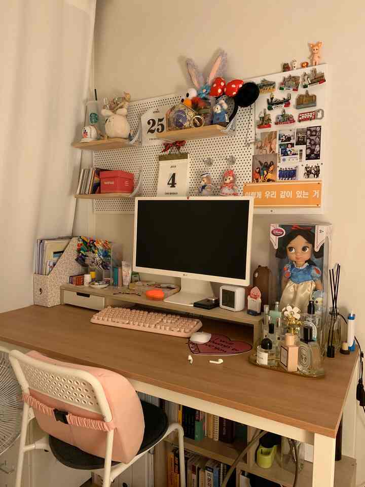 White-walled home office featuring a pegboard backdrop, a brown desk with monitor and assorted collectibles in a cozy single-user workspace
