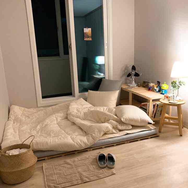 Beige and wood tone compact studio bedroom featuring floor bedding and wooden furniture, creating a cozy atmosphere