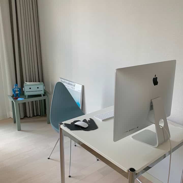 White and gray toned bedroom and home office space featuring a simple desk, Apple iMac, and a Drop Chair in a minimal design